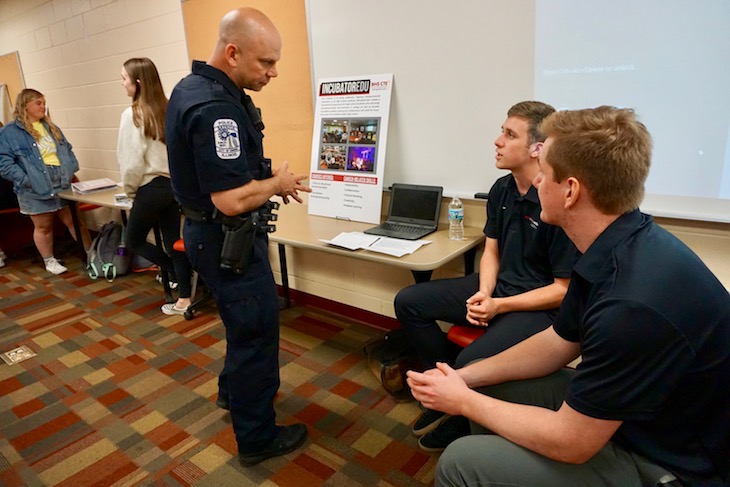 <p>Batavia Police Officer Justin Howe learning about the BHS INCubator Entrepreneurship program from two students who started their own company, Navigamers, LLC, through the INCubator program. </p>
