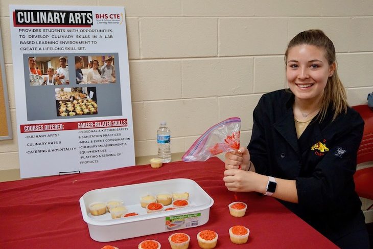 <p>Multitasker! Culinary Arts student sharing information about the program while frosting cupcakes. </p>
